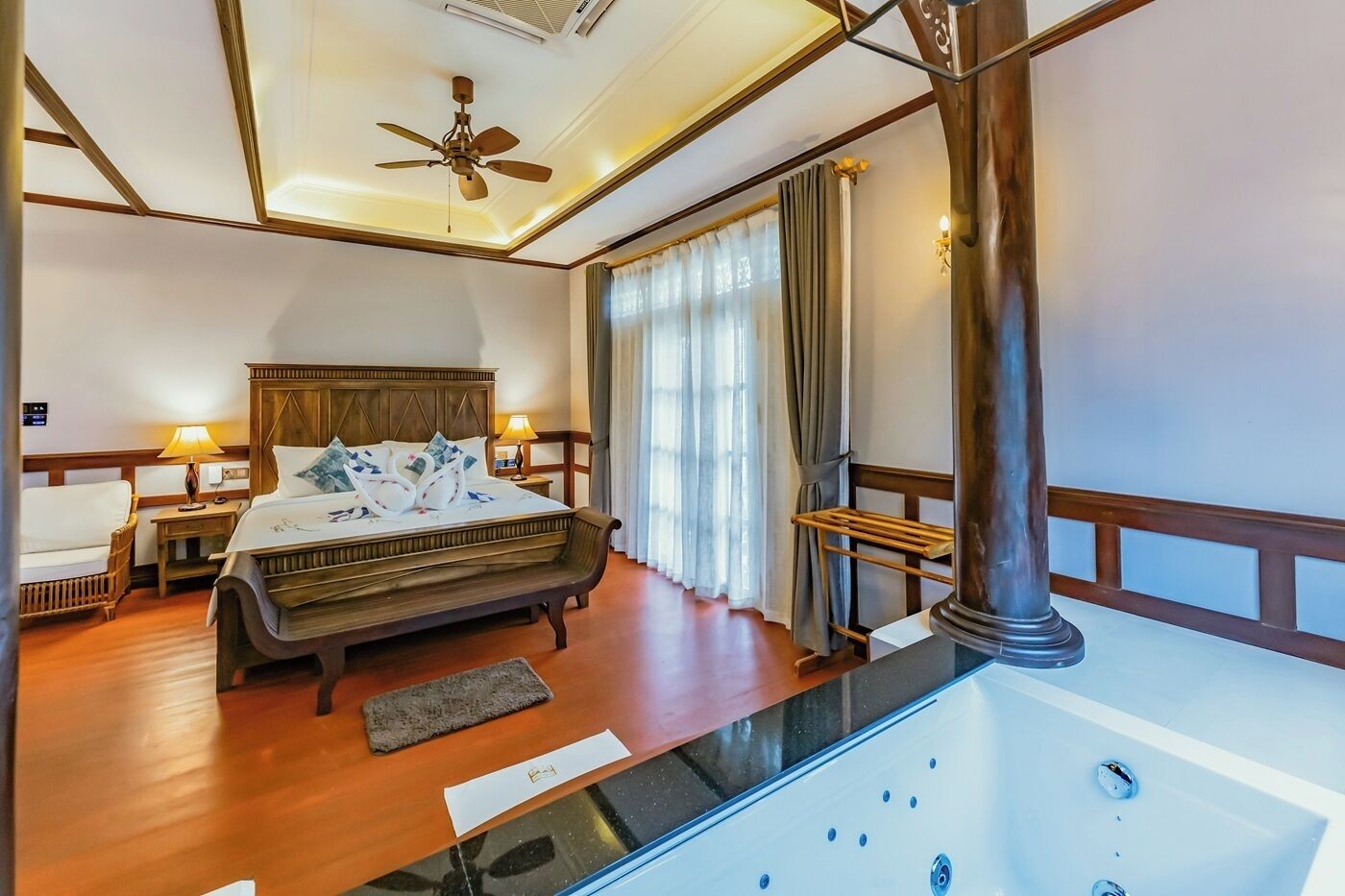 A hotel room with a large bed, a ceiling fan, a view of a pool, and a wooden floor.
