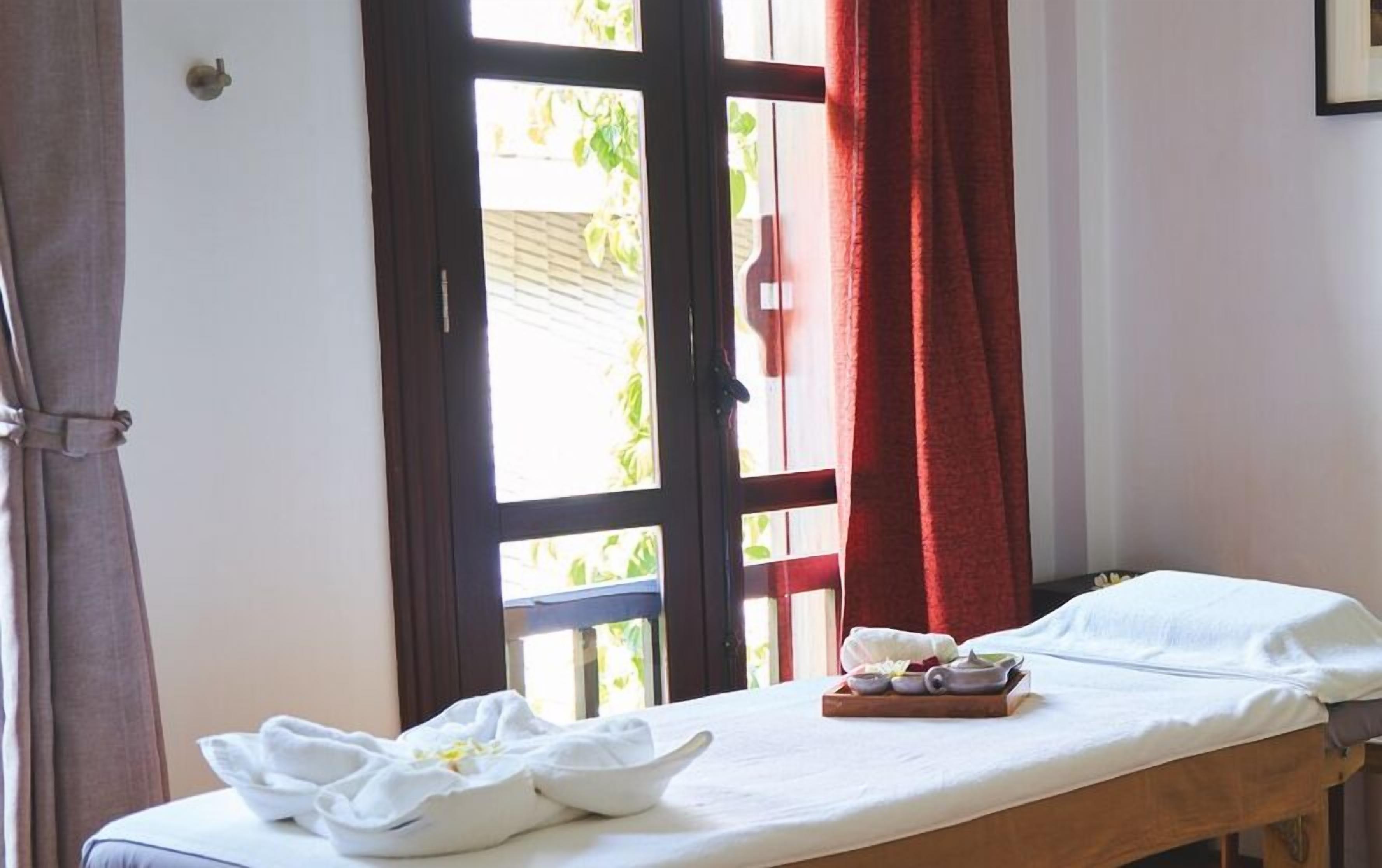 A room with a bed, a window with curtains, and a tray with towels and a bowl.
