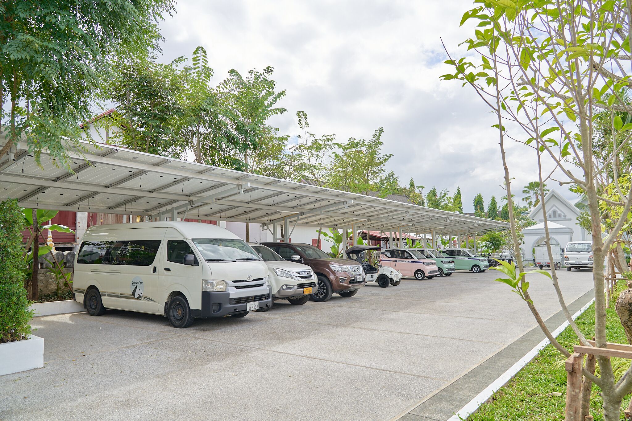 A parking area with several vehicles, including vans and cars, under a covered structure.