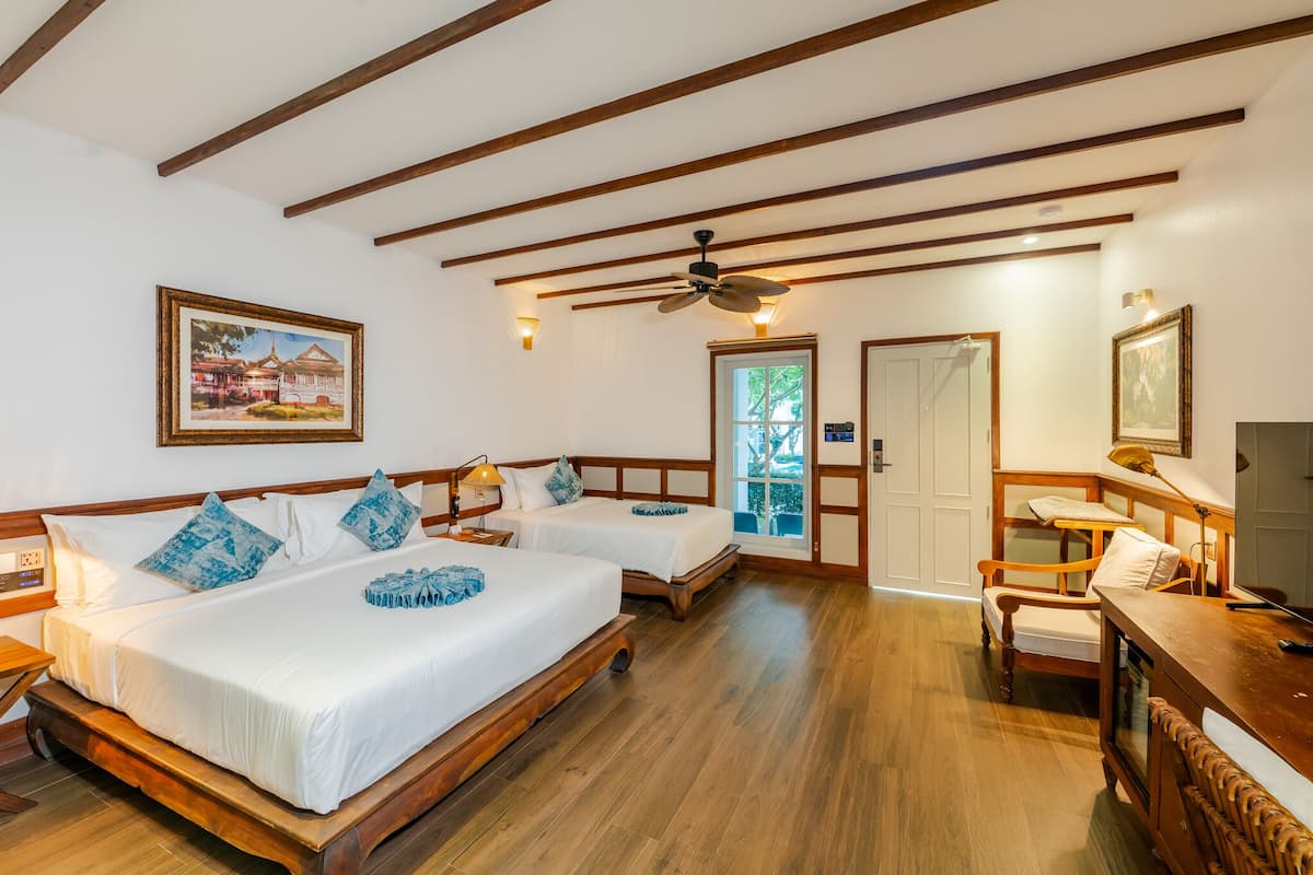 Een hotelkamer met twee bedden, houten vloeren, een plafondventilator en een televisie.