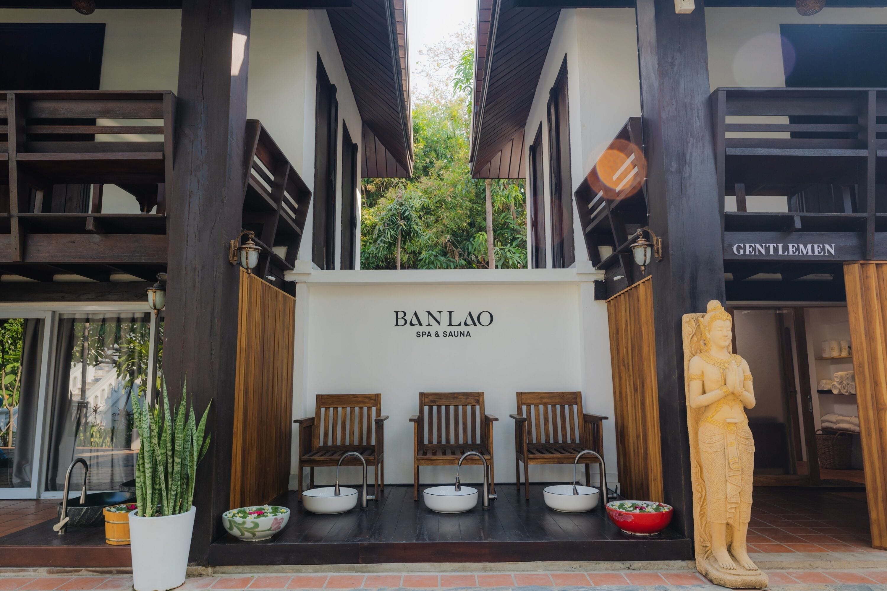 A spa entrance with a wooden bench seating area, a statue, and a sign reading "BANLAO SPA & SAUNA".