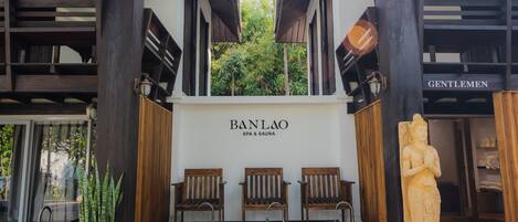A spa entrance with a wooden bench seating area, a statue, and a sign reading "BANLAO SPA & SAUNA".