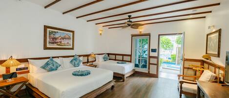 Habitación de hotel con dos camas, pisos de madera, ventilador de techo y vista a la vegetación.