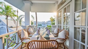 Un balcón con sillas de mimbre y una mesa lista para comer, con vistas a una zona residencial con palmeras y casas.