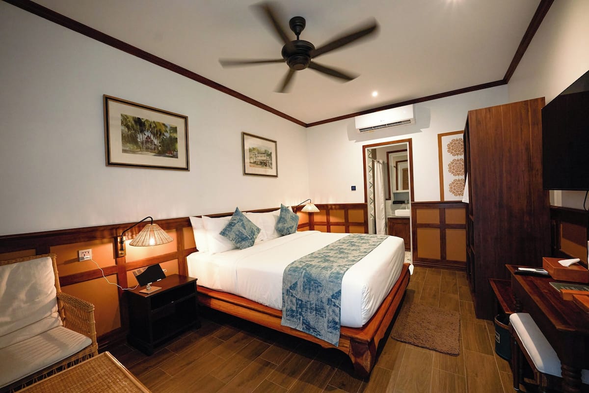 Hotelkamer met een bed, een bureau, een stoel, een plafondventilator en foto's in lijsten aan de muur.