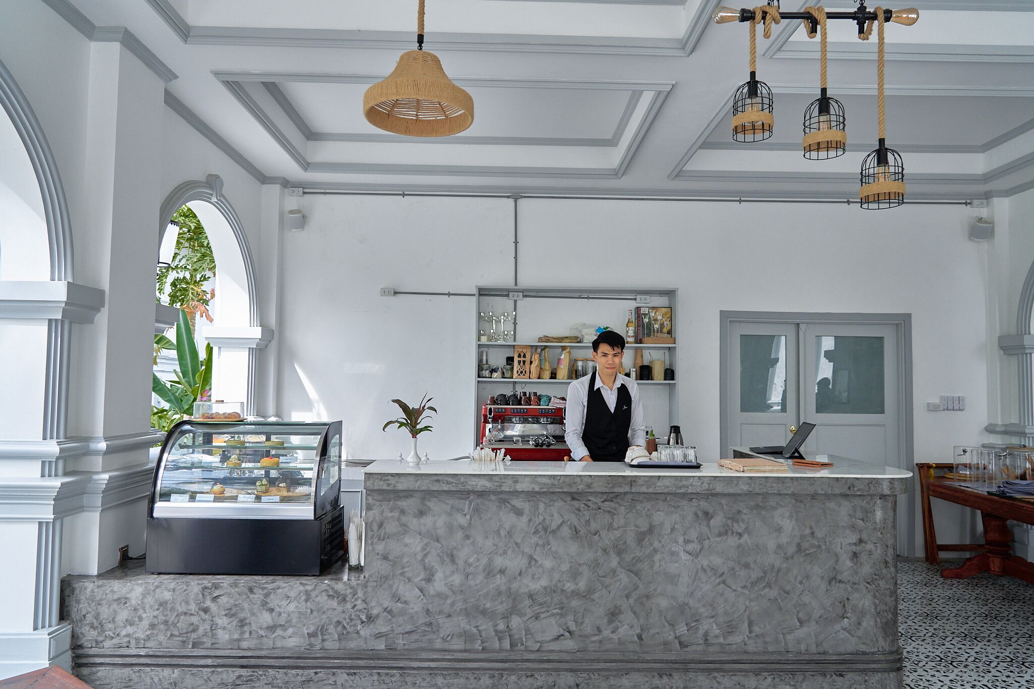 A marble counter with a coffee machine, a display case with pastries, and a person standing behind it.