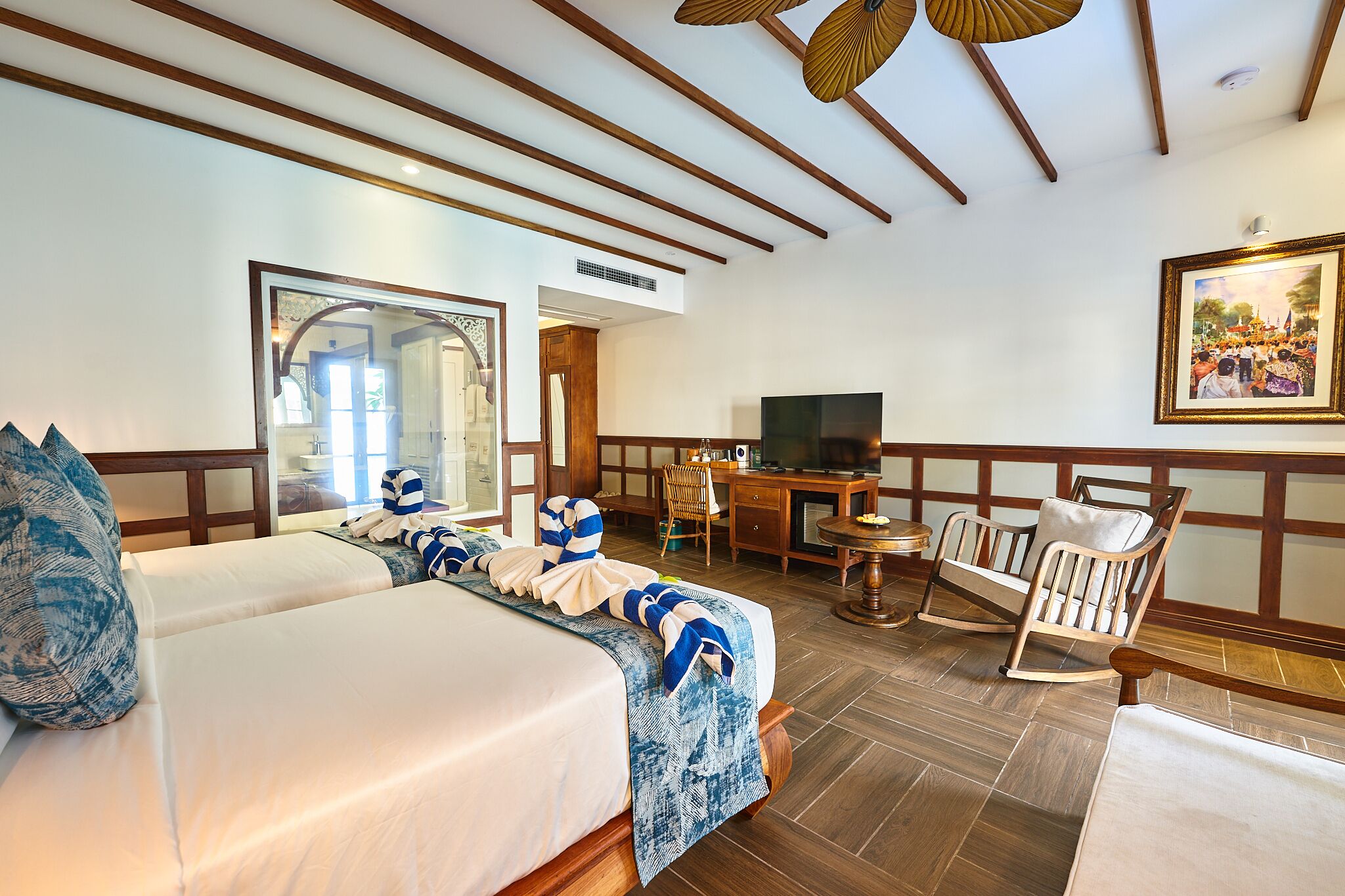 Quarto de hotel com uma cama grande, uma escrivaninha com televisão, uma cadeira de balanço e um quadro na parede.