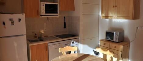 A compact kitchen with wooden cabinets, a microwave, a sink, and a dining table with chairs.