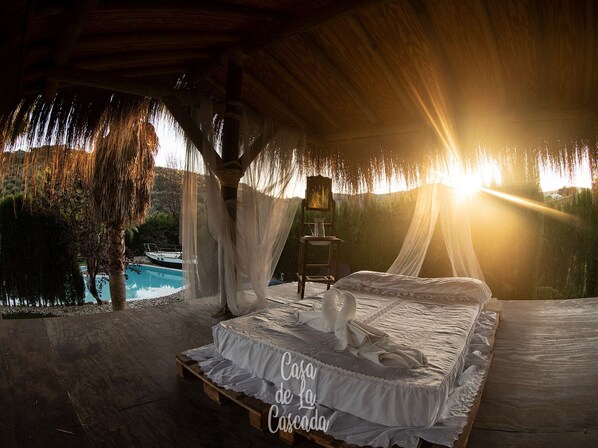 A bedroom with a bed, a small table, and a chair, with a view of a swimming pool outside.