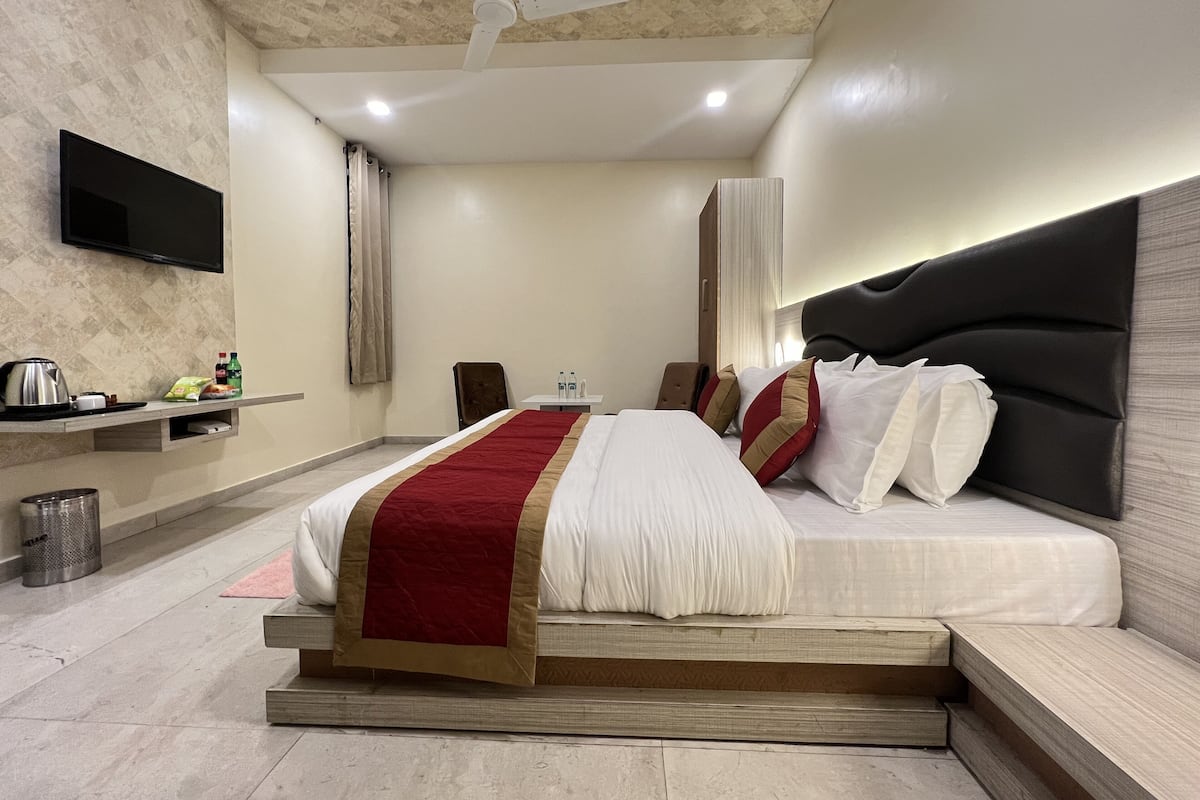 Ein modernes Hotelzimmer mit einem Bett, einem Flachbildfernseher, einem Deckenventilator und einem kleinen Tisch mit Wasserkocher und Snacks.