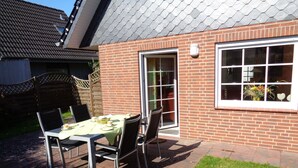 A patio with a table set for two, surrounded by chairs, and a brick wall with a window.