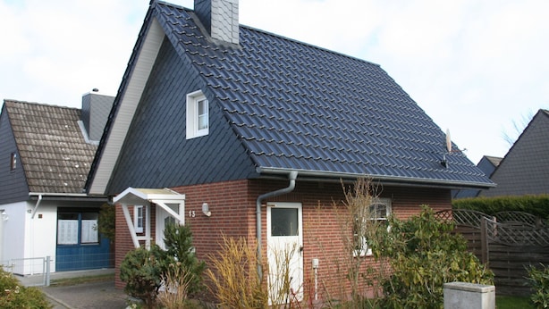 A residential house with a steeply pitched roof, a visible chimney, and a small porch.