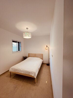 Un dormitorio con una cama de madera, una ventana, una lámpara de techo y una lámpara de pie.