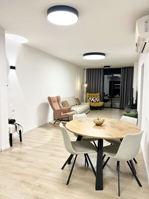 Una sala de estar moderna con una mesa de comedor redonda de madera, sillas blancas, un sofá color beige y un sillón rosa.