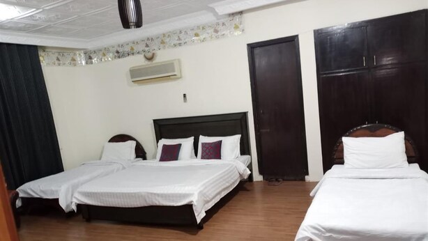 A hotel room with two beds, wooden flooring, a ceiling fan, an air conditioning unit, and a wardrobe. - Premier Lodge (Islamabad)