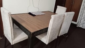A dining table with four upholstered chairs, a power outlet on the wall, and a dark wooden floor. - Premier Lodge (Islamabad)