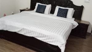 A bedroom with a dark wooden bed, white bedding, and a wall-mounted air conditioner. - Premier Lodge (Islamabad)