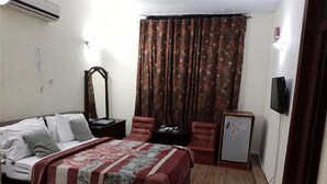 A bedroom with a bed, a desk, a chair, a mirror, and a television. - Premier Lodge (Islamabad)