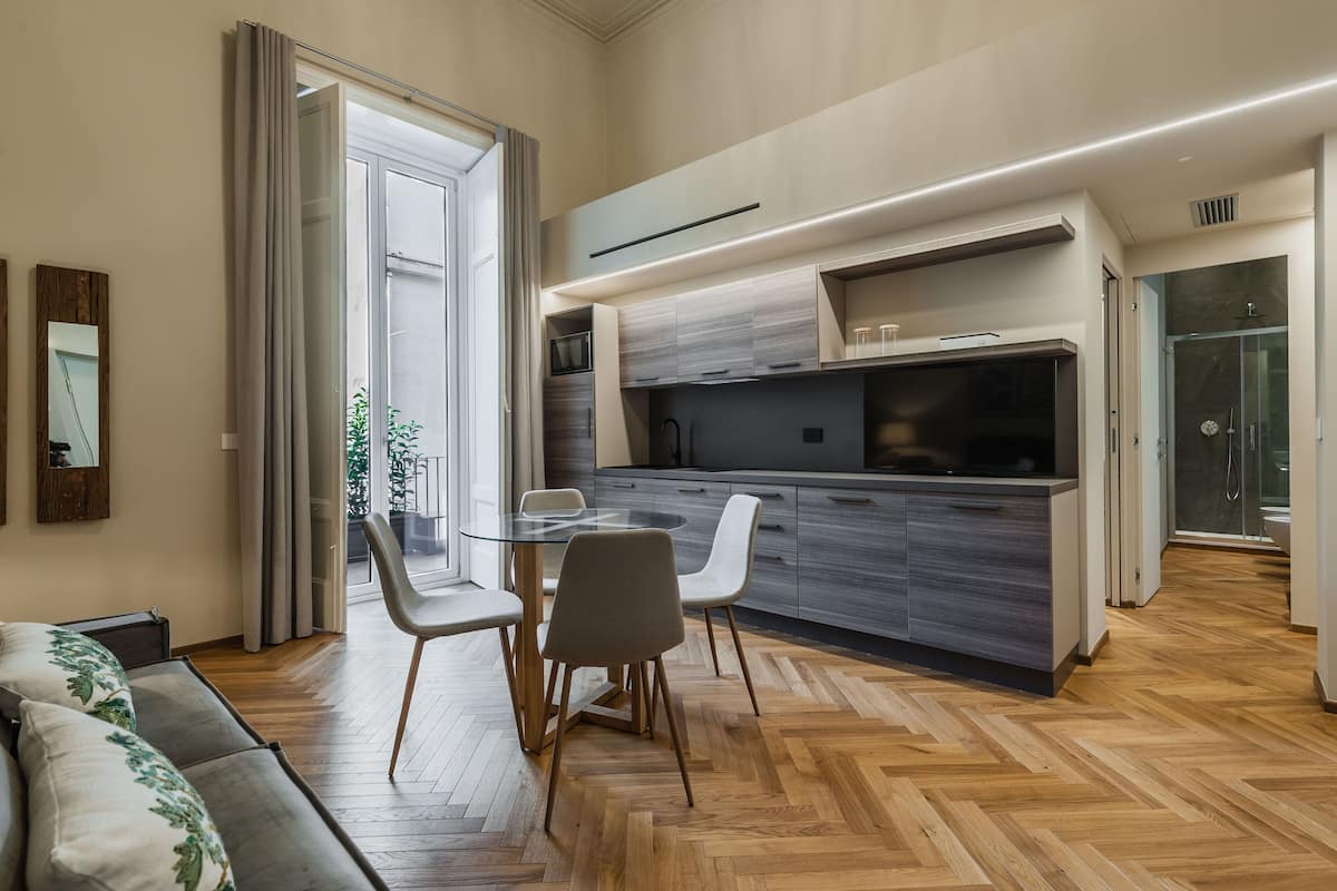 A modern kitchen with a dining area, wooden flooring, and a glass door leading to a balcony.