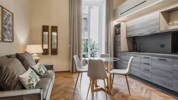Una sala moderna con un sofá, una mesa redonda y sillas. Se observa una zona de cocina con armarios y encimera.