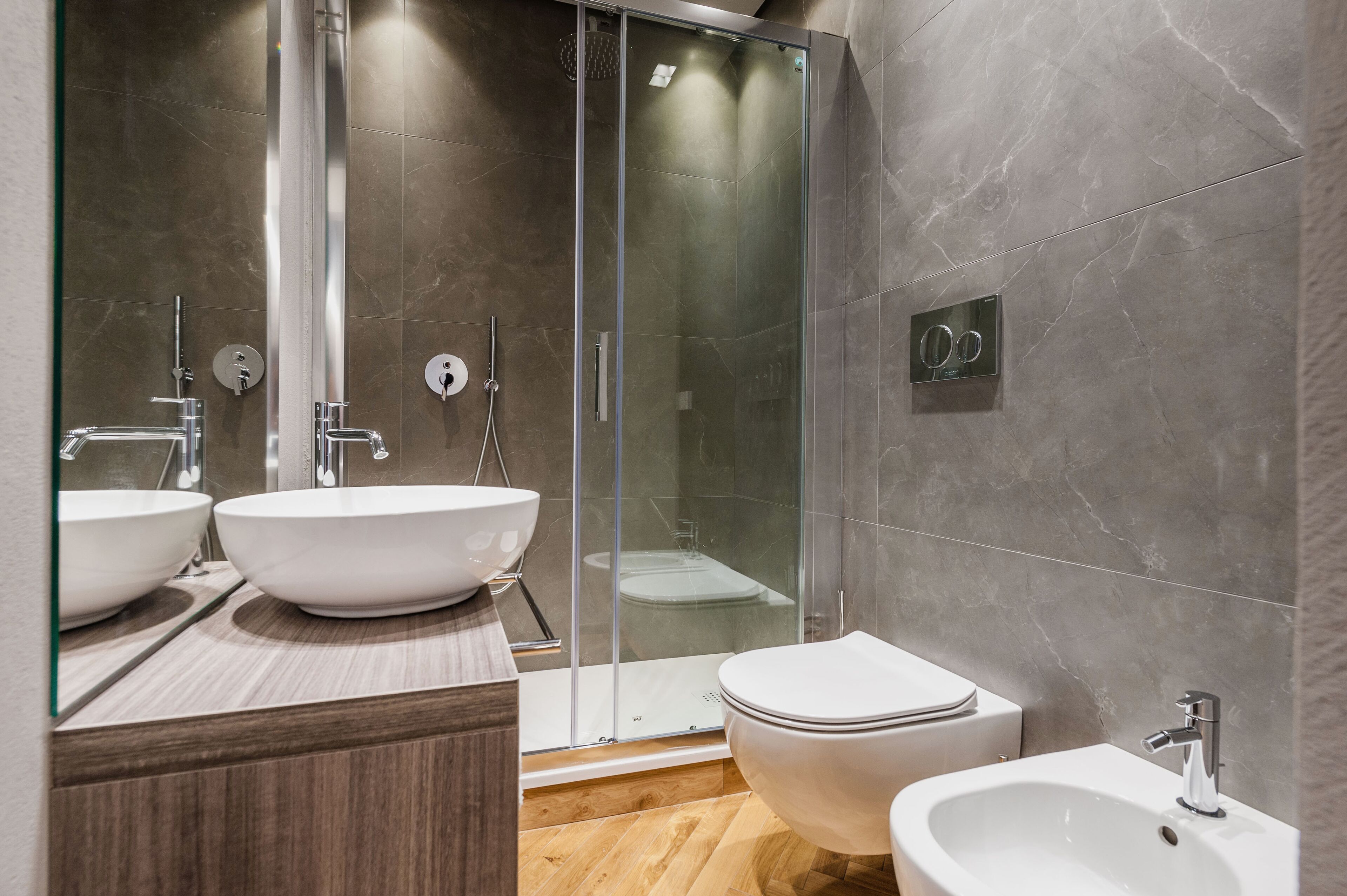 Un baño moderno con dos lavamanos grandes de color blanco, una ducha con cerramiento de vidrio, un inodoro y un bidé.