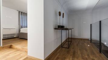 A modern hotel room with a wooden floor, a bed, a standing heater, and a small table with two decorative items.