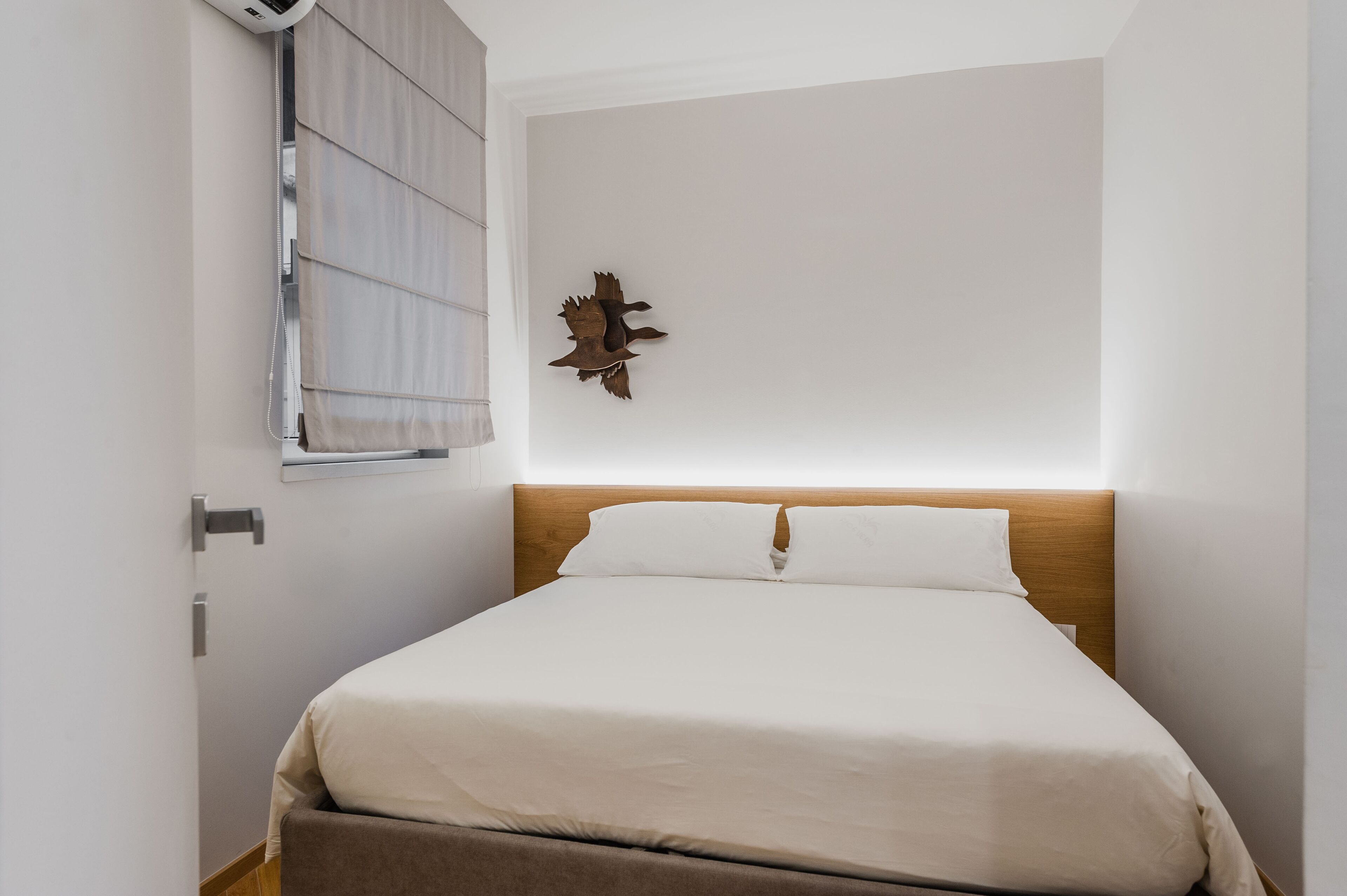 Habitación de hotel con una cama, cabecera de madera, una obra de arte en la pared y una ventana con persianas.