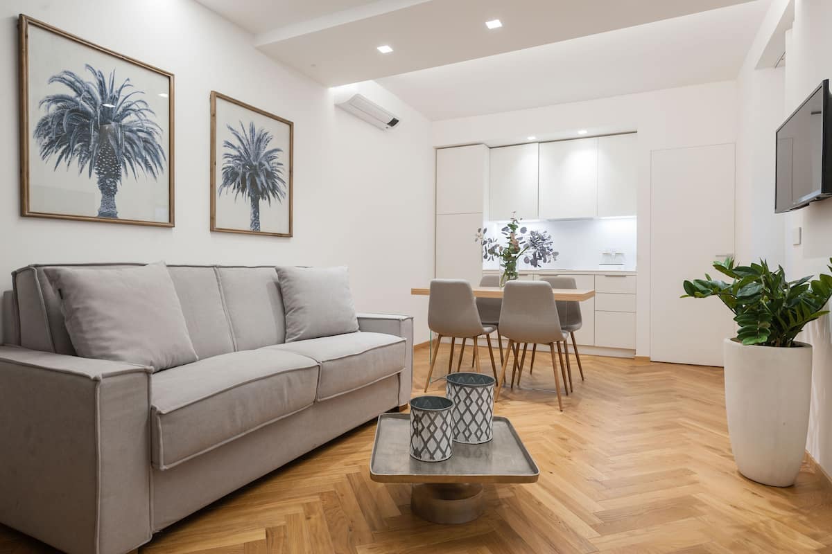 A modern living room with a grey sofa, a dining table with chairs, and a kitchen in the background.