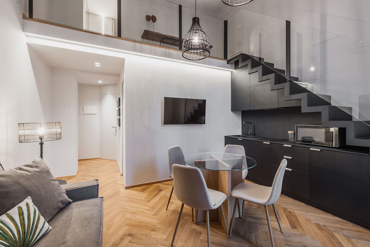 A modern kitchen with a glass dining table, grey chairs, and a black staircase.