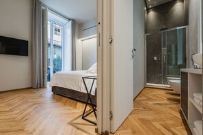 A modern bedroom with a bed, a TV, and a bathroom with a shower and toilet. - Ferrini Home - Riso 80 (Catania)