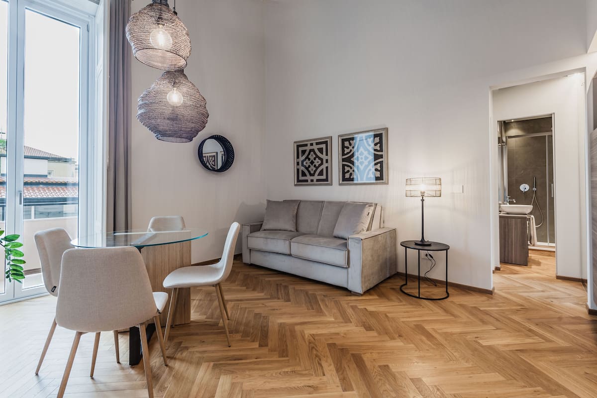 A modern living room with a glass-top dining table, grey sofa, and a small side table.