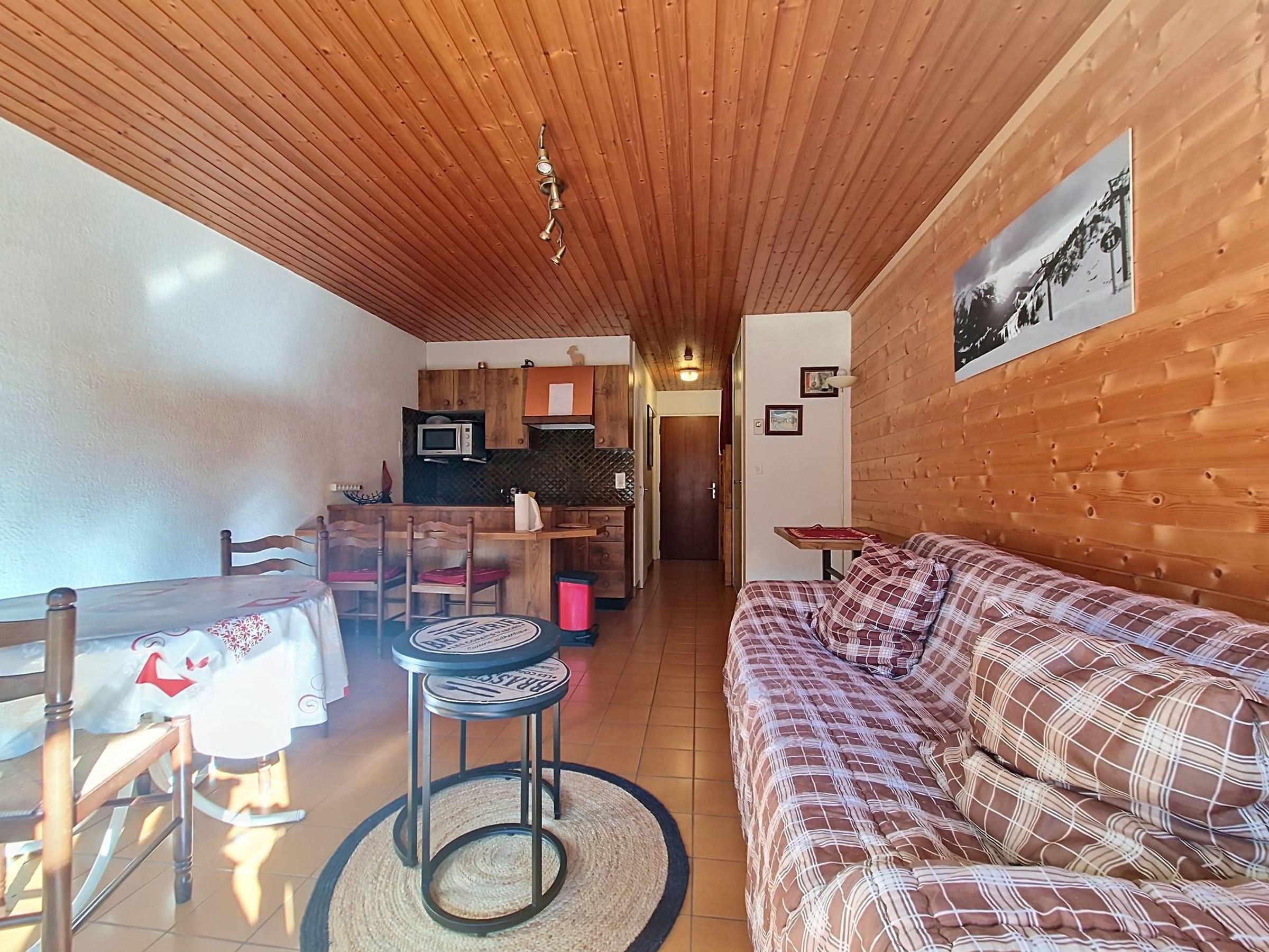 Un intérieur chaleureux avec un plafond en bois, un coin repas avec des chaises et une table, un canapé, une cuisine équipée d’un four à micro-ondes et un tableau encadré au mur.