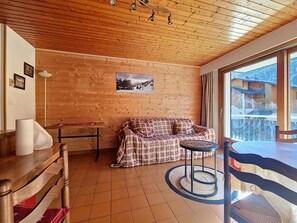 Une pièce chaleureuse avec un plafond en bois, un canapé à carreaux, une petite table et une vue sur les montagnes par une grande fenêtre.