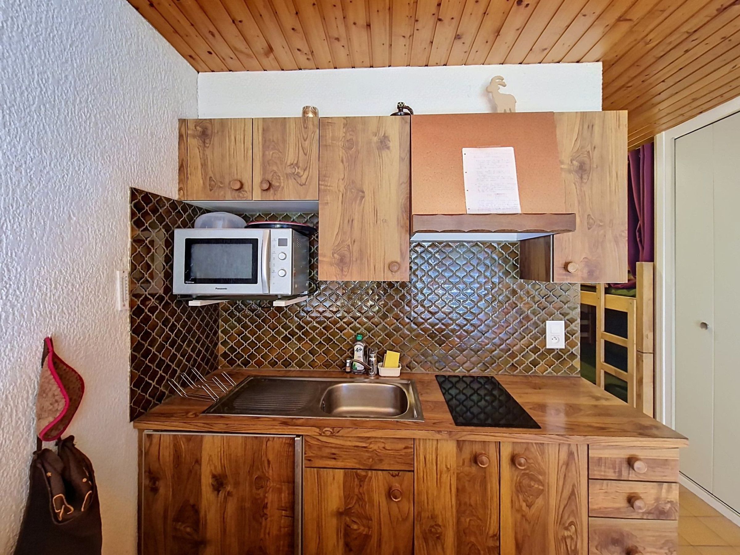 Cozinha compacta com armários de madeira, micro-ondas, pia e bancada pequena.