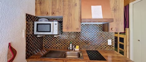 Cozinha compacta com armários de madeira, micro-ondas, pia e bancada pequena.