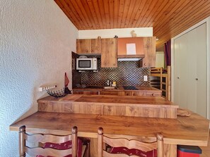 Une cuisine compacte dotée de meubles en bois, d’un four à micro-ondes et d’un coin repas avec une table et des chaises en bois.