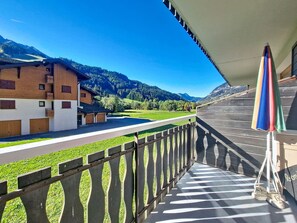 Un balcon offrant une vue sur un paysage montagneux, une clôture en bois et un parasol coloré.