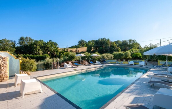 Une piscine entourée de verdure et d’un mur de pierre, avec des chaises longues et des parasols.