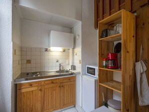 Una cocina compacta con armarios de madera, un lavamanos de acero inoxidable, un microondas y una cafetera sobre un estante de madera.