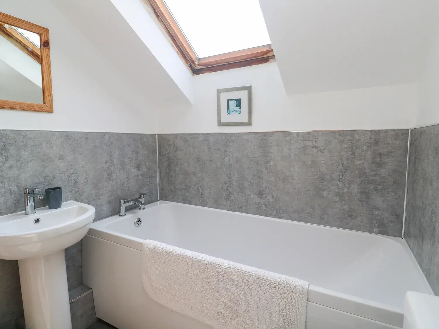 A modern bathroom with a skylight, a bathtub, and a sink.