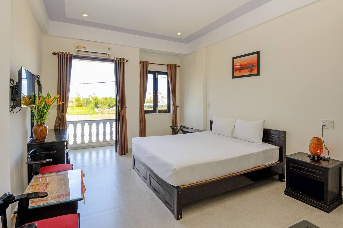 Une chambre d’hôtel avec un lit, un bureau et une chaise, une télévision et une fenêtre avec des rideaux.