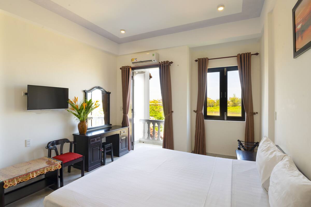 Une chambre d’hôtel comprenant un lit, un bureau avec une chaise, un téléviseur fixé au mur et une fenêtre avec des rideaux.