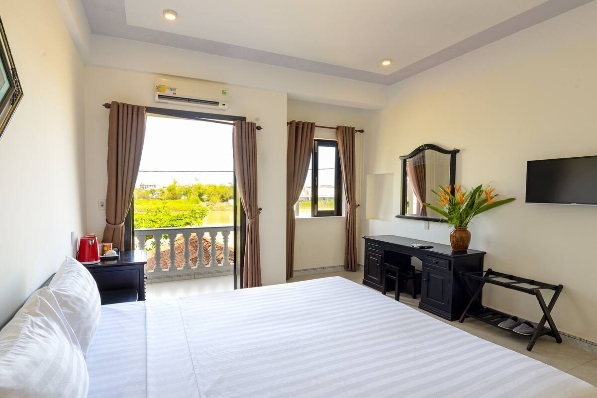 Une chambre d’hôtel avec un lit, un bureau, une chaise, une télévision et un balcon avec des rideaux.