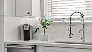 A modern kitchen with a built-in coffee maker, a potted plant, and a stainless steel sink. - Cottage Evergreen: Outdoor Grille, Patio w/ Putt! (Mesa)