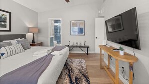 A modern bedroom with a bed, bedside table, TV, and a ceiling fan. - Cottage Evergreen: Outdoor Grille, Patio w/ Putt! (Mesa)