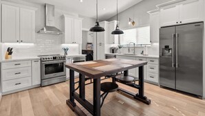 A modern kitchen with white cabinetry, stainless steel appliances, and a central island with stools. - Cottage Evergreen: Outdoor Grille, Patio w/ Putt! (Mesa)