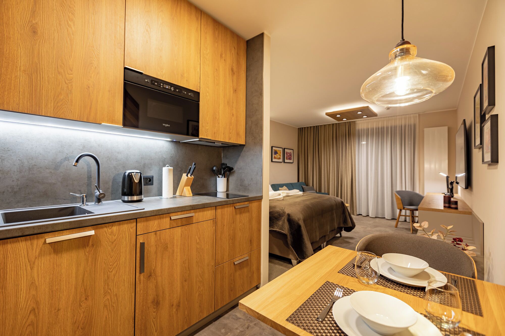 A modern kitchen with wooden cabinets, a built-in oven, and a dining area with a table set for two.