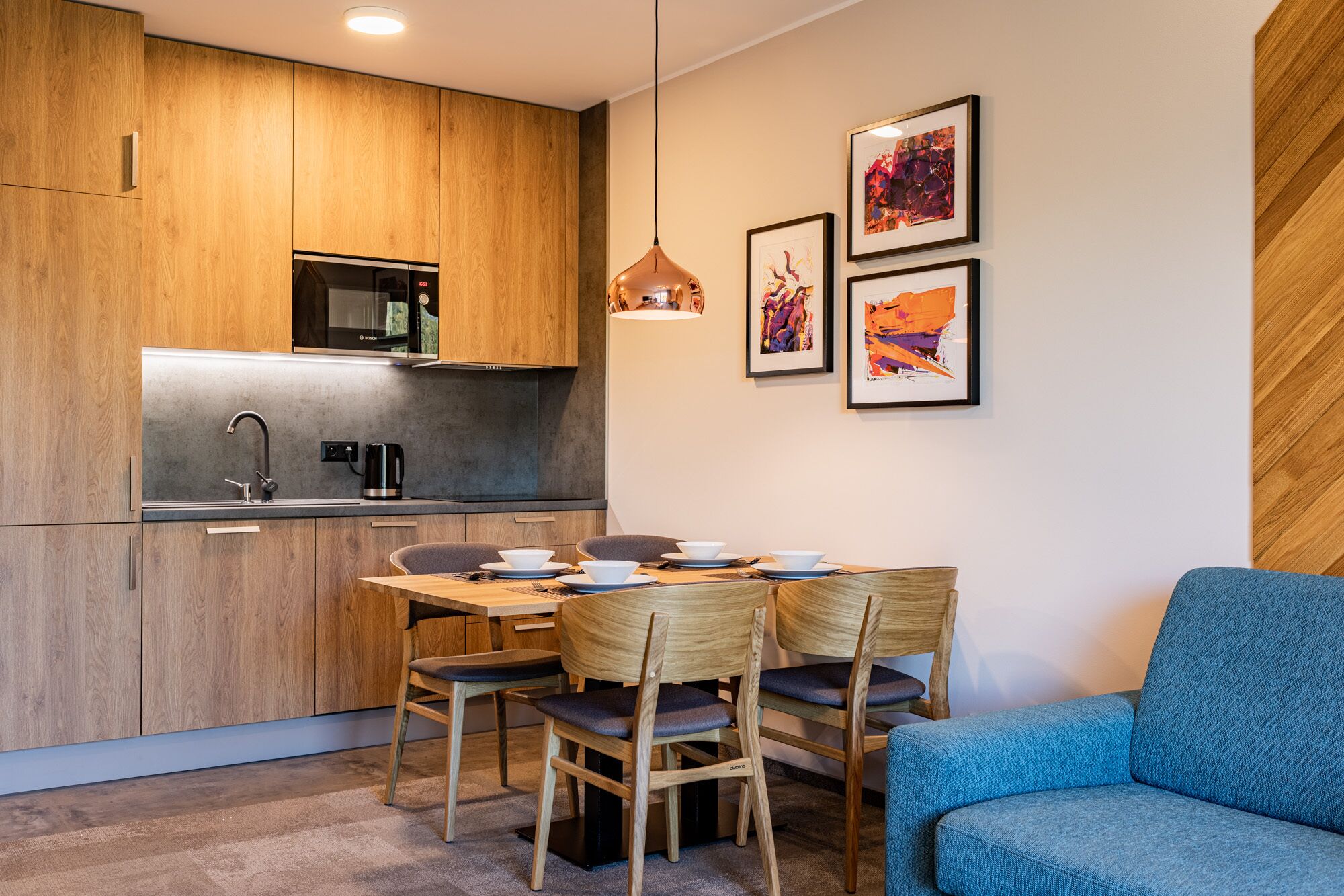 Une cuisine moderne avec des meubles en bois, un four à micro-ondes de la marque Bosch et un coin repas comprenant une table et des chaises.