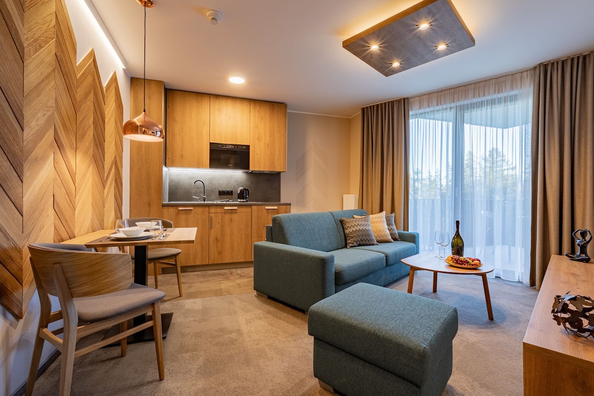A modern living room with a sofa, ottoman, and a dining table with a vase and wine bottle.