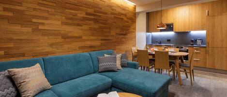 A modern living room with a teal sofa, wooden wall paneling, and a dining area with a wooden table and chairs.